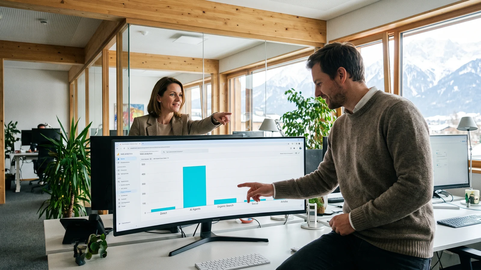 Im hellen Büro eines Tiroler Hotelbetriebs zeigen die Marketingleiterin und ein Kollege auf einen Monitor, auf dem der Balken für AI Agents alle anderen Besucherquellen überragt